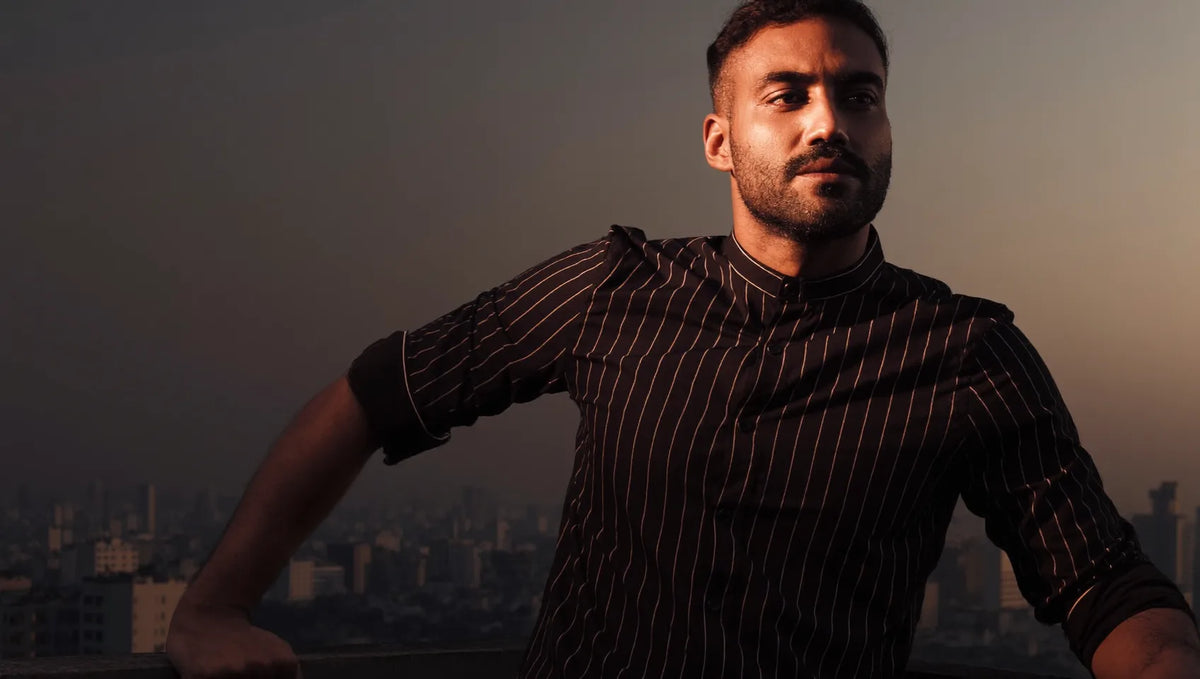 A man in a black pinstripe Marvén shirt on a Dhaka rooftop at sunset